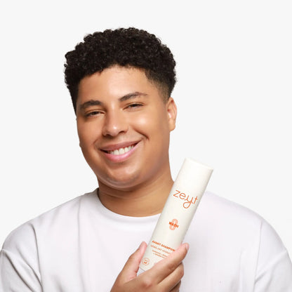 Homme souriant tenant une bouteille d'avant-shampoing hydratant "Wash 0" de la marque Zeyt. Le produit est formulé avec des ingrédients naturels pour démêler et hydrater les cheveux.