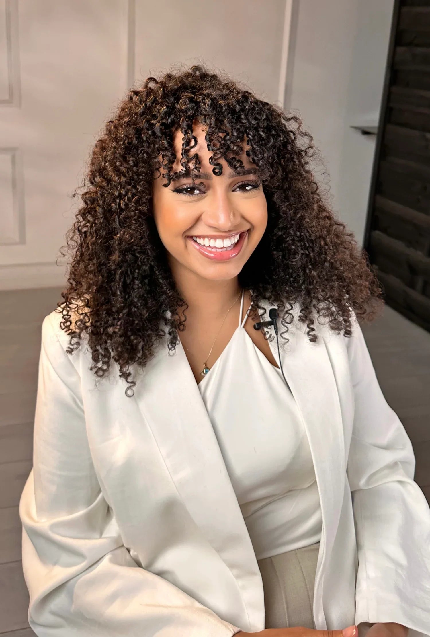 Femme souriante aux cheveux bouclés portant un blazer blanc